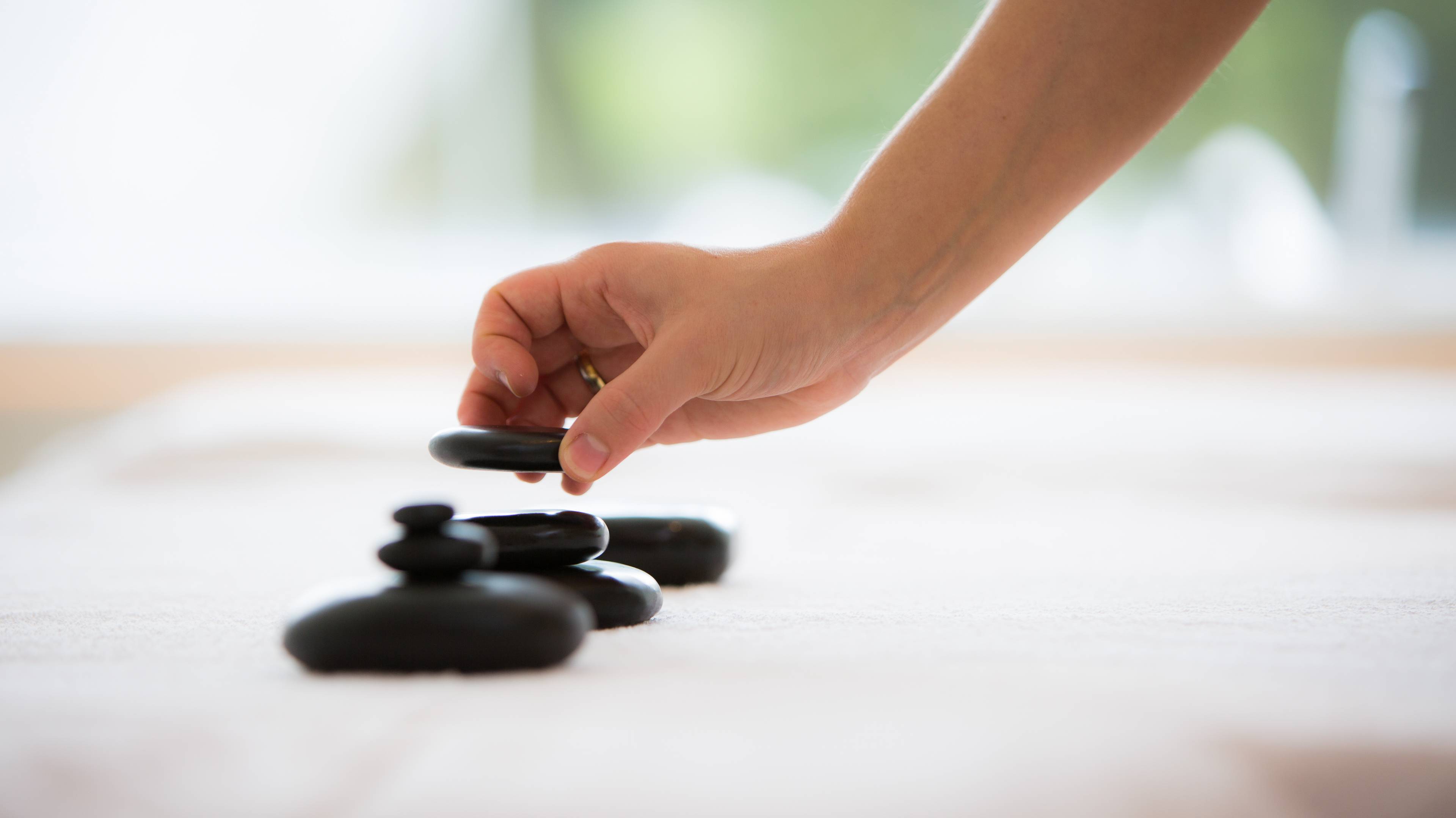 Eine Hand stapelt schwarze flache Steine aufeinander